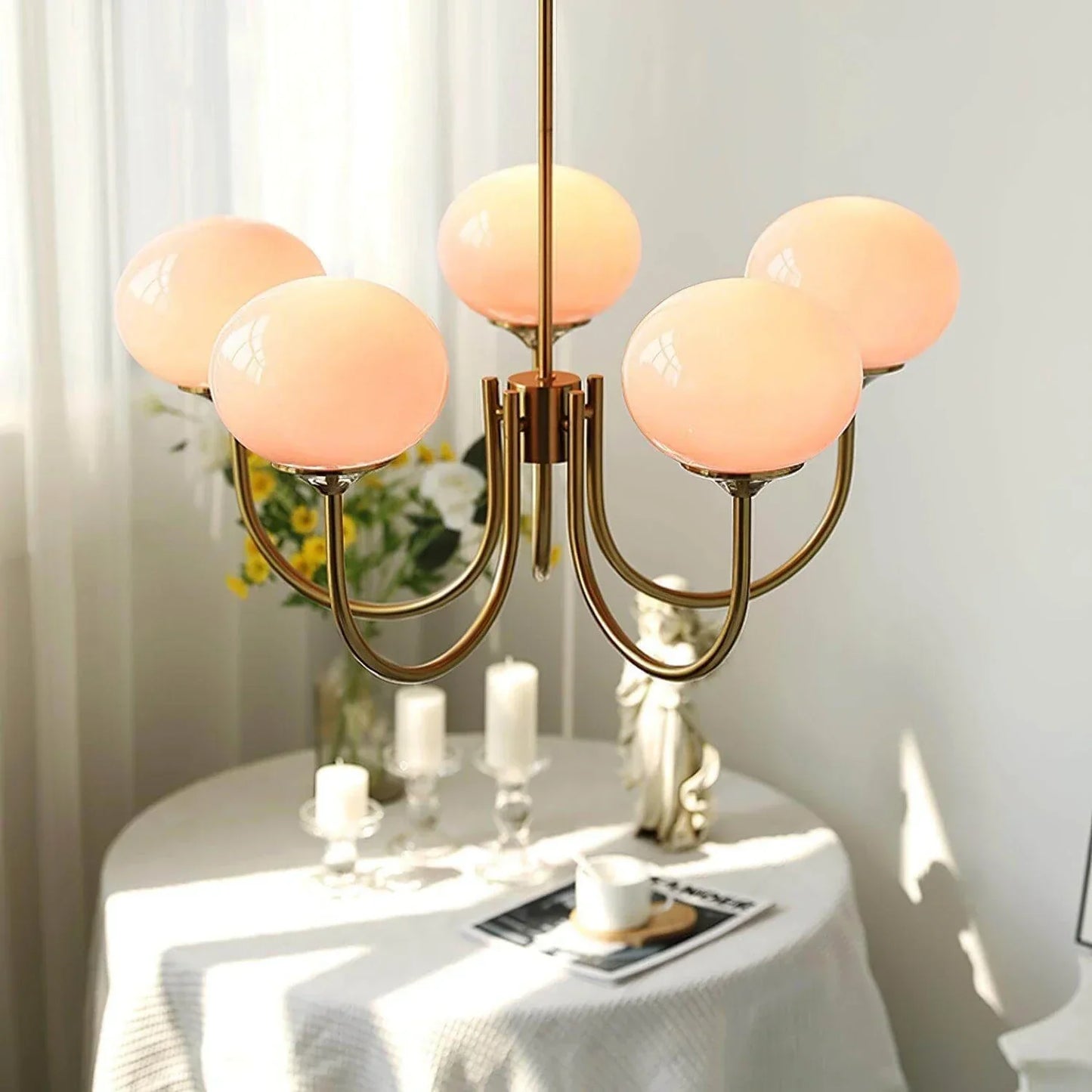 Modern brass pendant ceiling light featuring five pink glass ball globes, hanging in a bright interior above a table with candles.