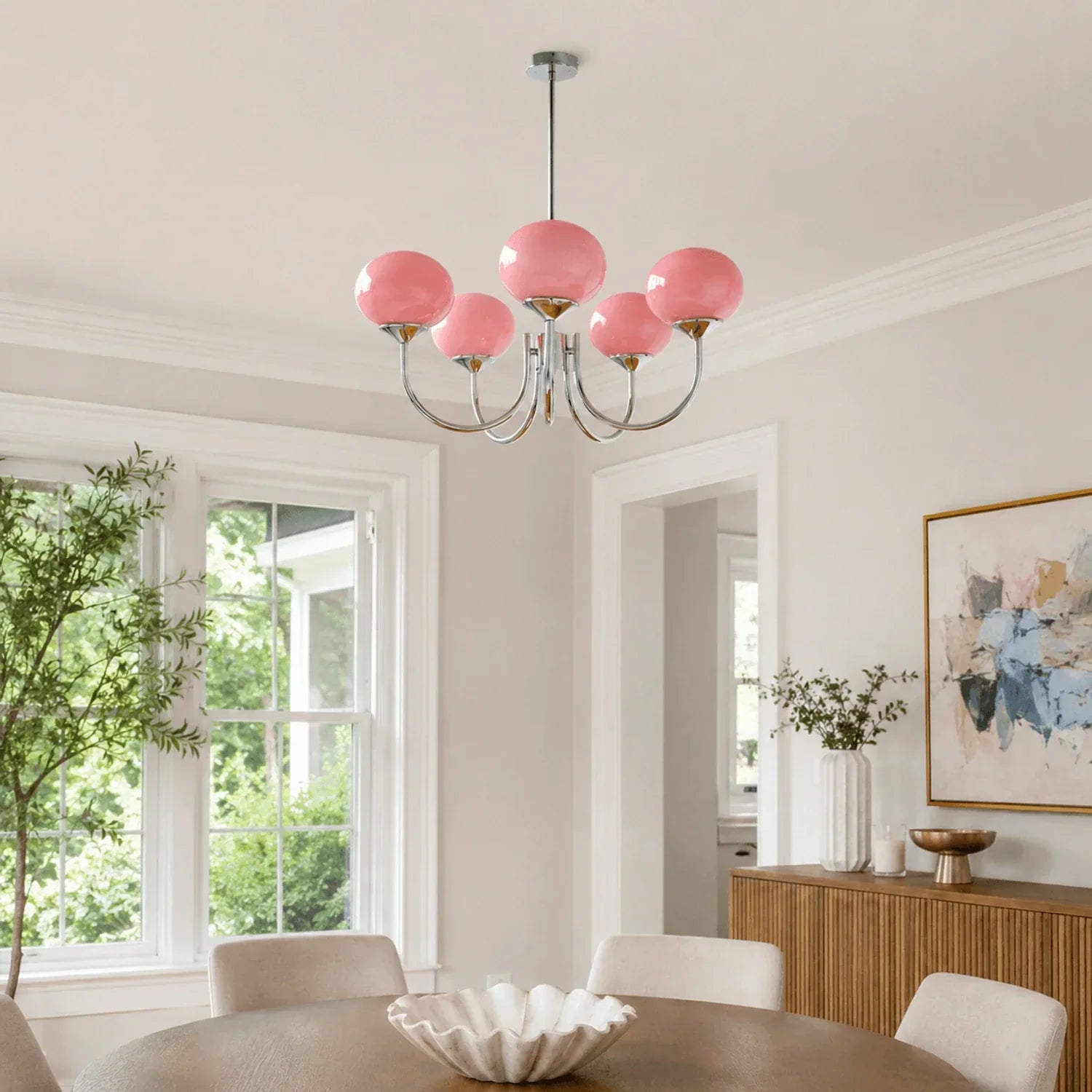 A modern five-light pendant chandelier featuring pink glass ball globes and a polished chrome metal finish, hanging above a dining table.