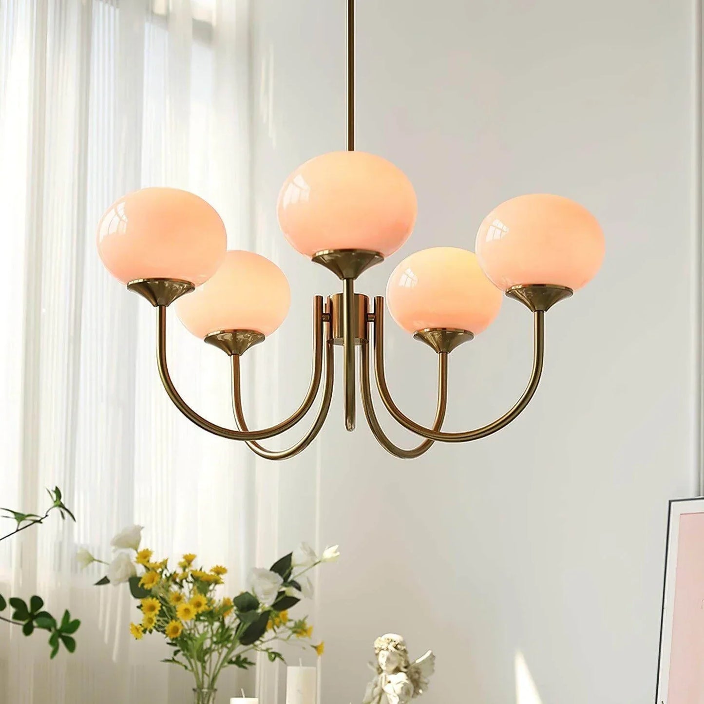 Modern five-arm pendant light featuring glowing spherical glass shades and a polished brass finish, suspended in a bright, contemporary living space.