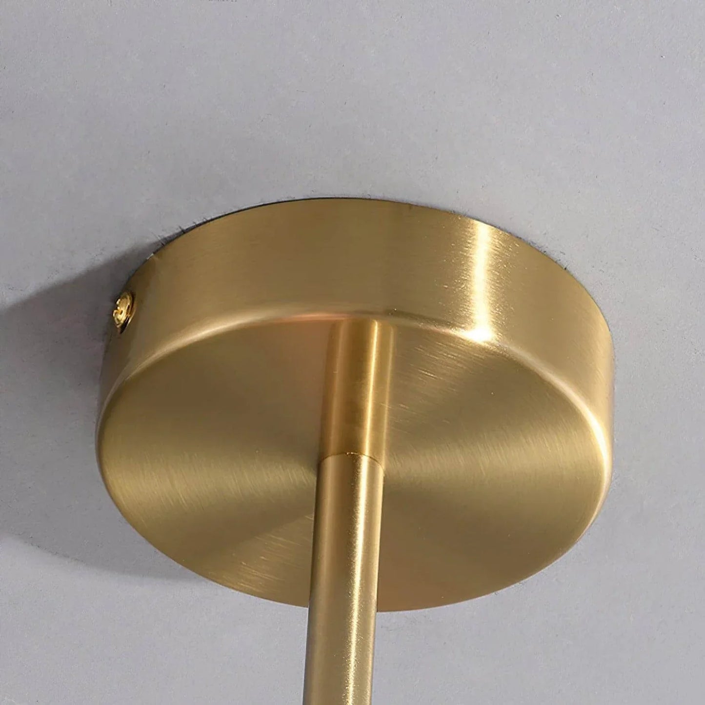 Close-up of the brushed brass ceiling rose and matching metal rod of the modern pendant light, shown mounted on a smooth grey ceiling.