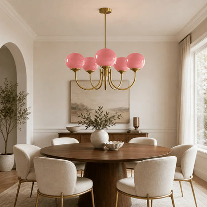 Modern brass pendant ceiling light with five pink glass ball shades, hanging above a round wooden dining table in a neutral-toned dining room.