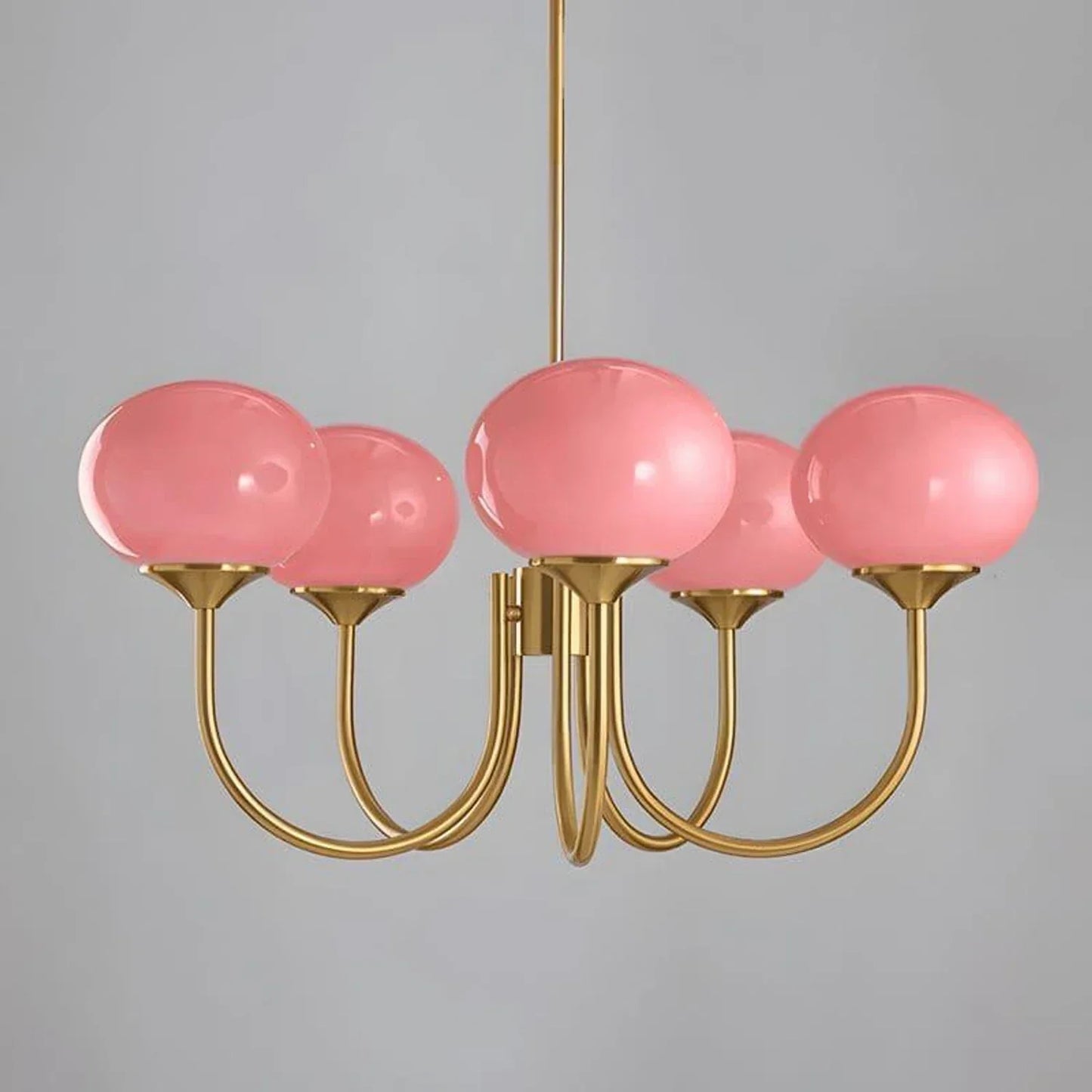 A modern glass ball pendant light featuring five curved brass metal arms, each supporting a glossy pink glass globe shade against a grey background.