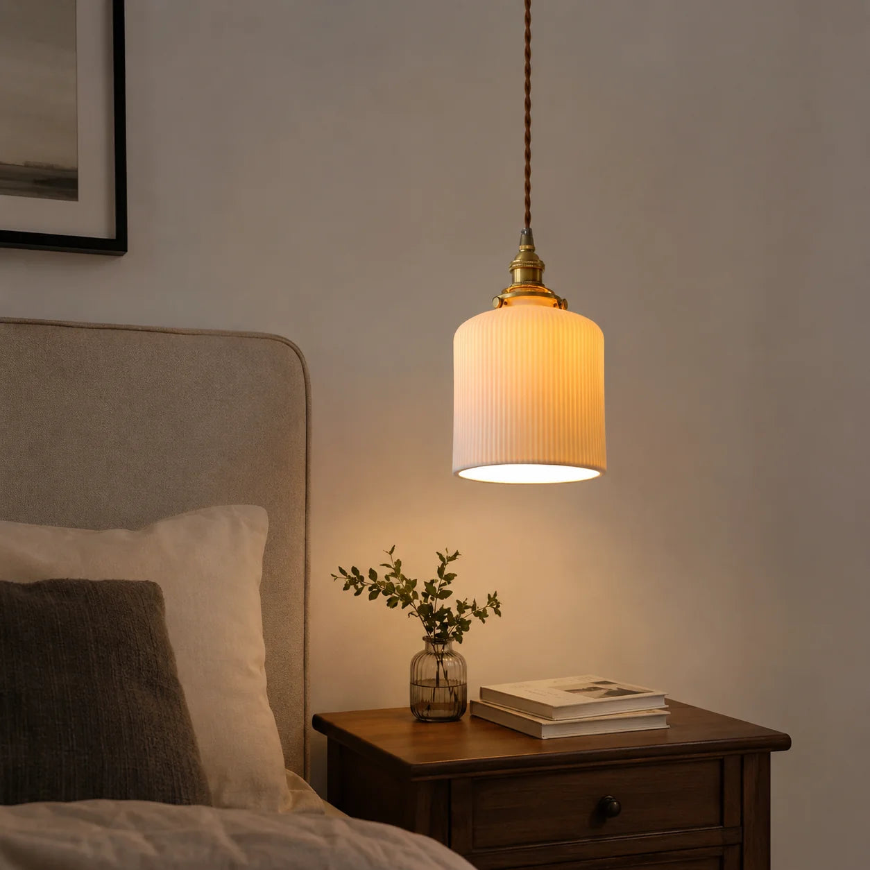 Modern ribbed glass pendant light with an adjustable cord and brass fitting, illuminating a bedside table with a warm glow in a contemporary bedroom.