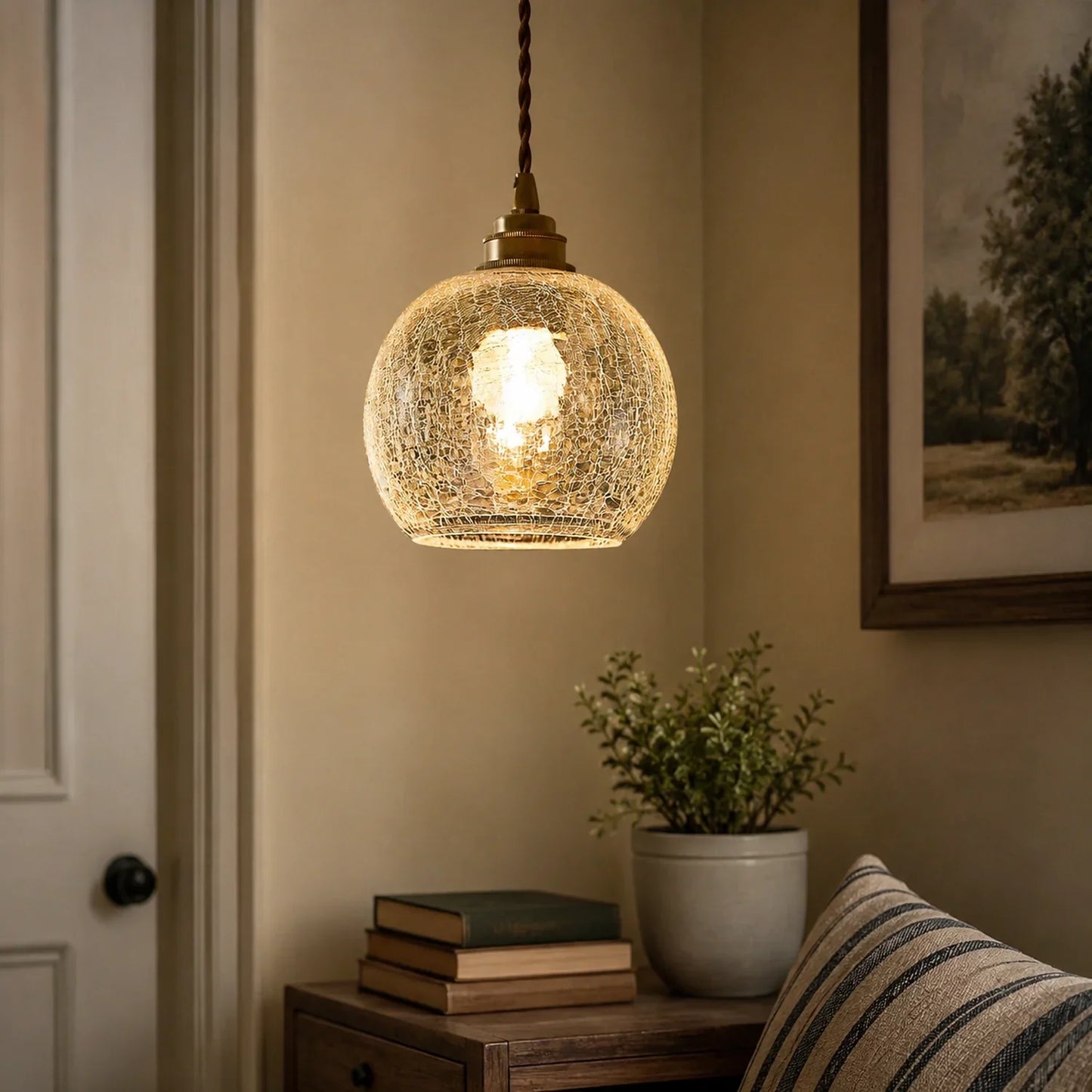 A modern glass pendant light with a crackle effect finish, hanging from an adjustable cord above a bedside table in a warm, cosy bedroom setting.