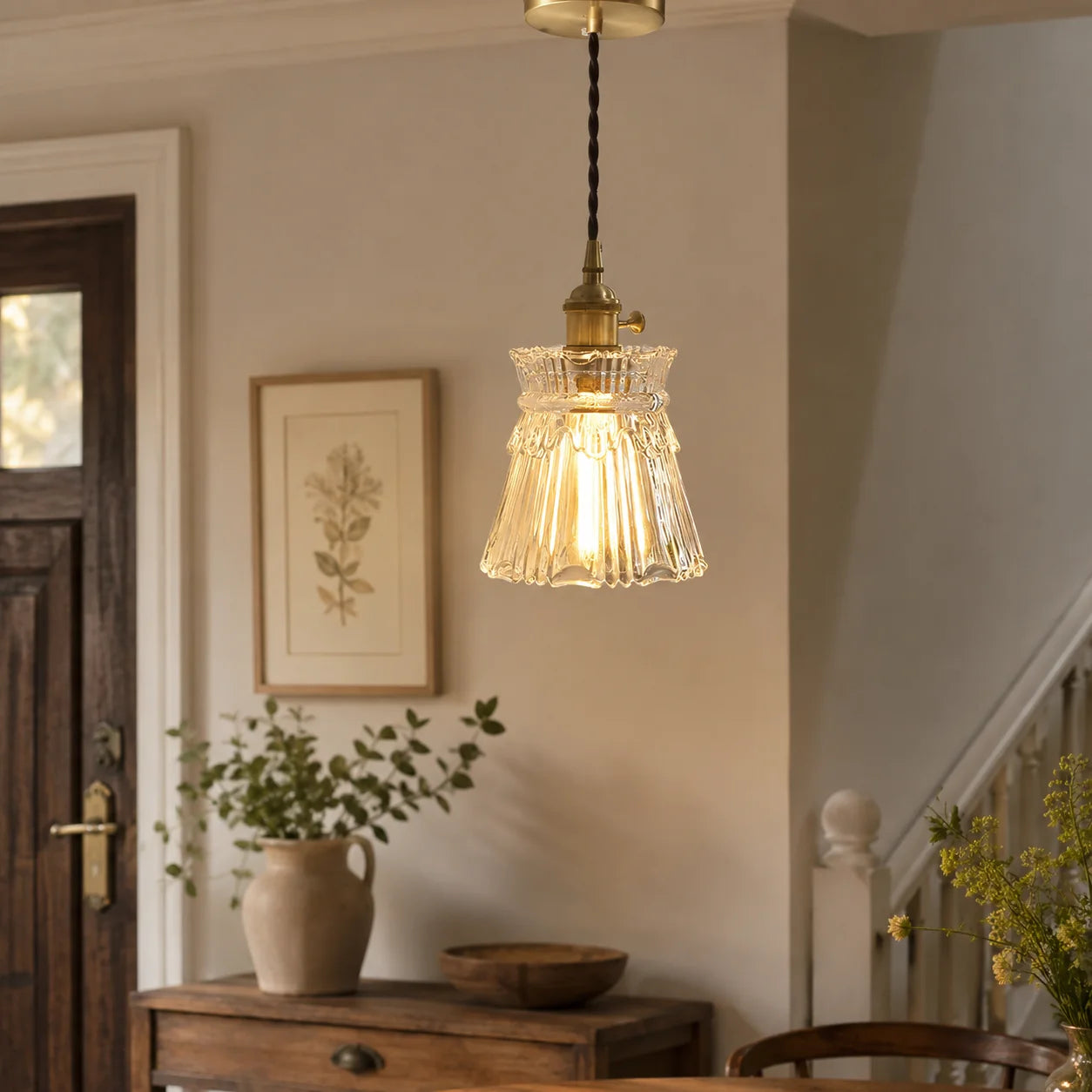 Clear glass pendant light with a fluted design and brass fitting, suspended by an adjustable cord in a warm, modern dining room interior.