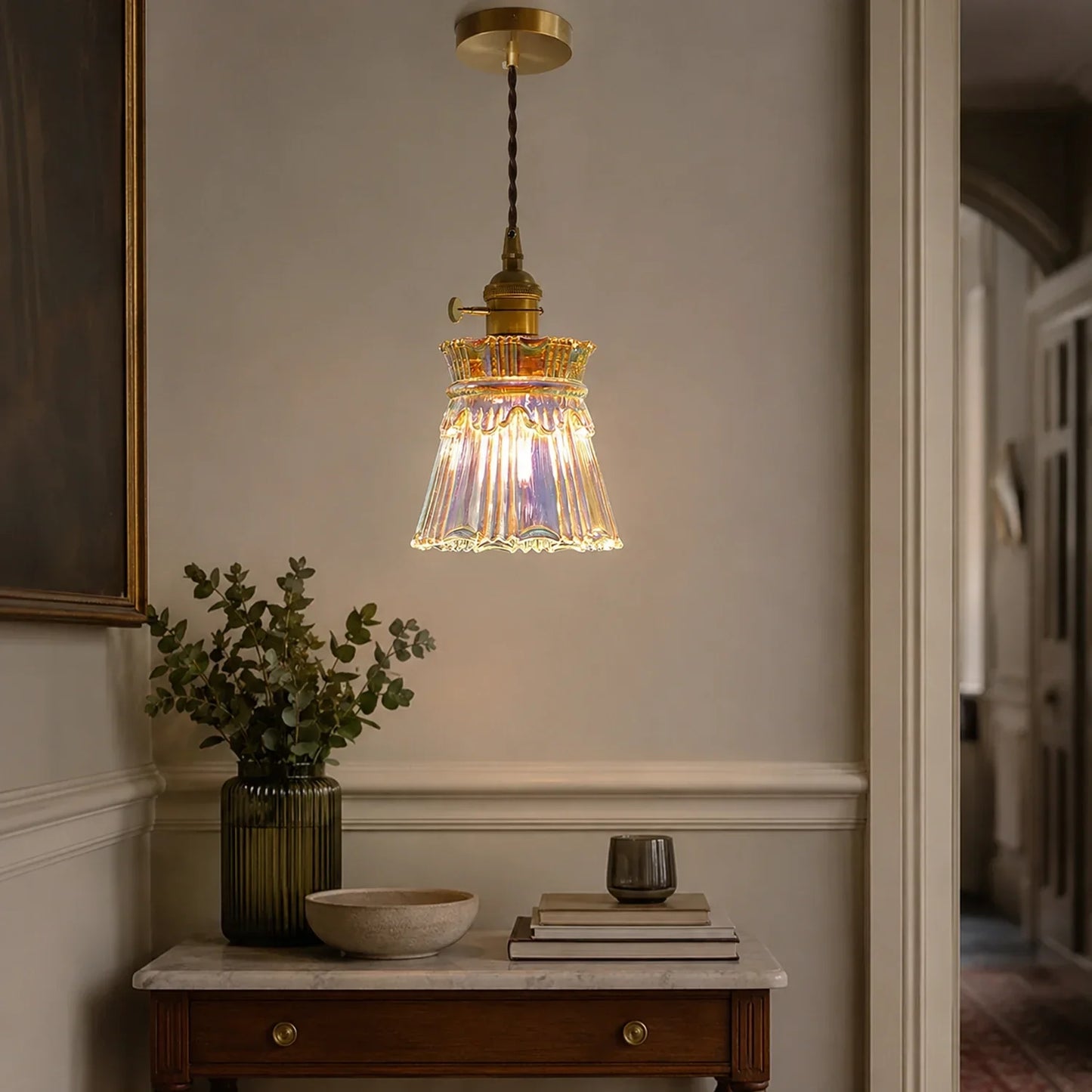 Modern glass pendant light with a colourful iridescent finish and brass fixture, hanging above a marble-topped console table in a stylish dining room.