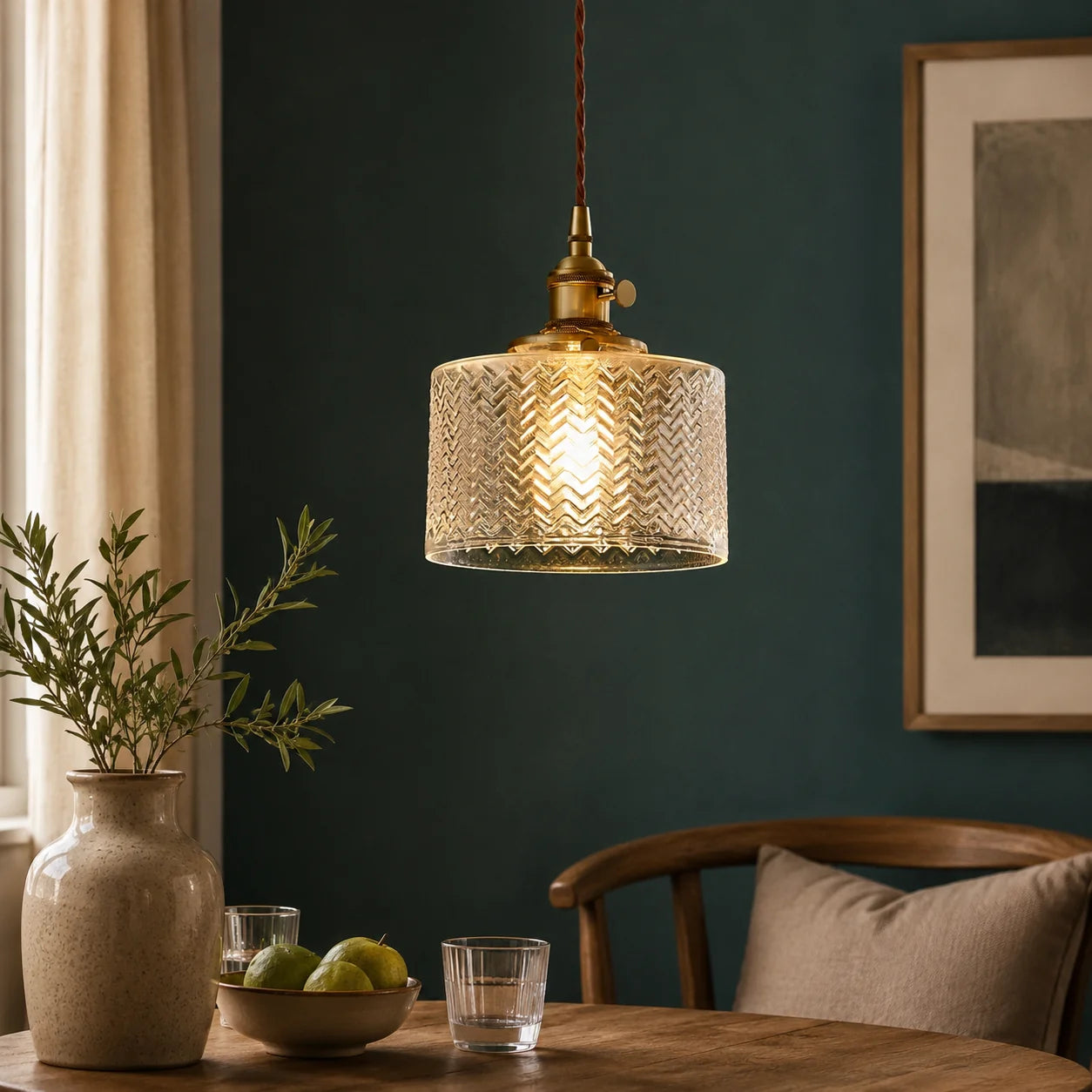Modern clear glass pendant light with a textured herringbone pattern and brass fitting, hanging above a wooden dining table in a stylish interior.