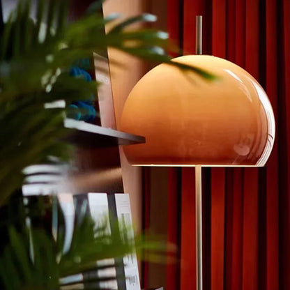 A mid-century modern floor lamp with a dome-shaped gradient orange glass shade, casting a warm glow in a stylish living room setting.