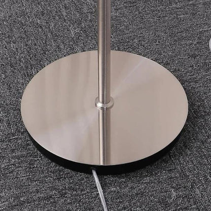 Close-up of the circular brushed metal base and stem of the Gradient Orange Glass Floor Lamp, resting on a textured grey carpeted floor.
