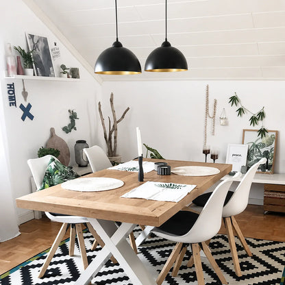Two black dome pendant lights with gold interiors hanging above a wooden dining table in a bright, modern kitchen with white chairs and decor.