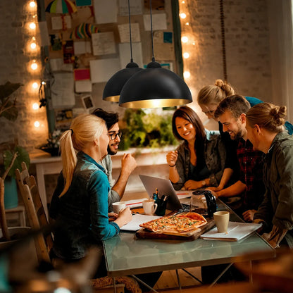 Two industrial dome pendant lights with black exteriors and gold interiors hanging above a group of friends socialising at a dining table.