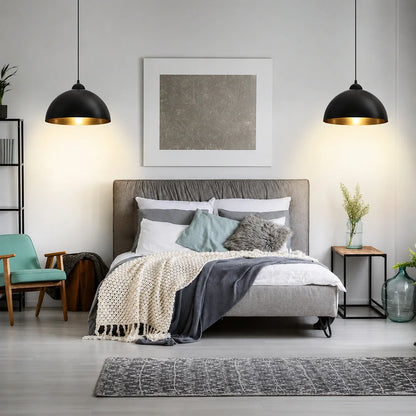Two black and gold industrial dome pendant lights hanging above a modern grey upholstered bed in a stylishly decorated bedroom interior.
