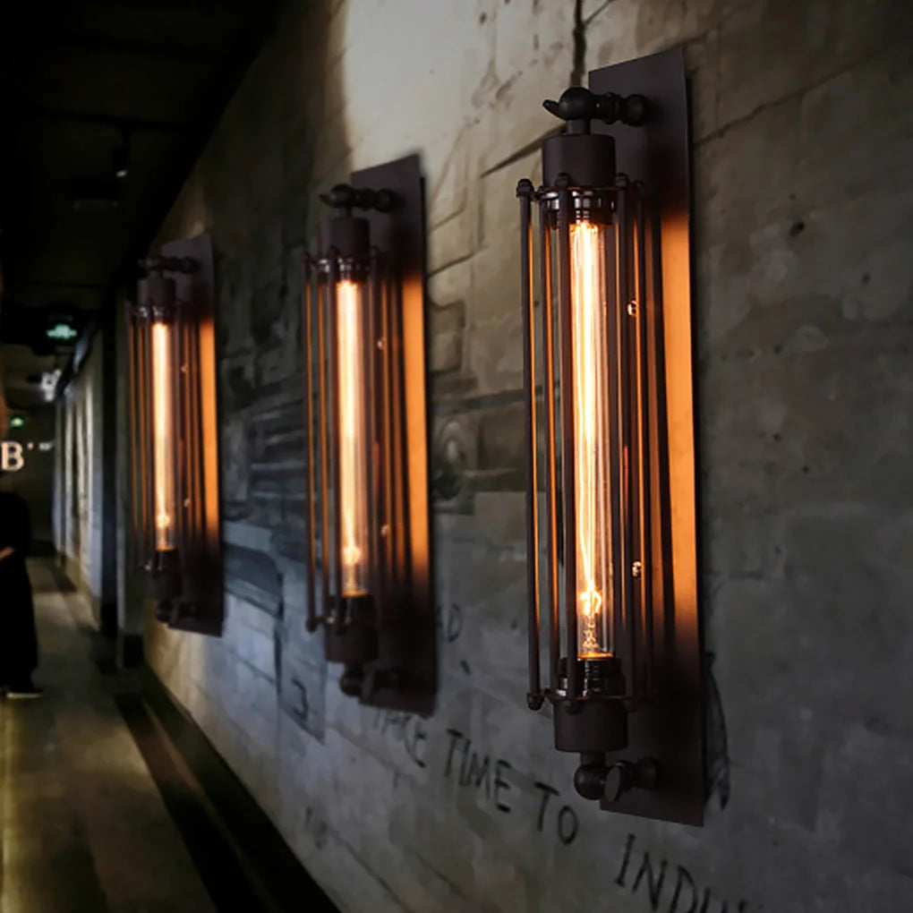 Three industrial iron wall sconces with vertical cage designs and glowing filament bulbs mounted on a textured brick wall in a loft-style corridor.