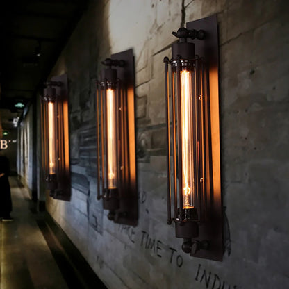 Three industrial iron wall sconces with vertical cage designs and glowing filament bulbs mounted on a textured brick wall in a loft-style corridor.