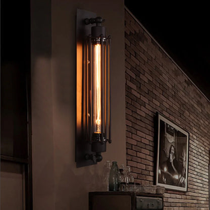 Vintage industrial iron wall sconce with a long, glowing filament bulb mounted on a dark wall in a loft-style room with exposed brickwork.