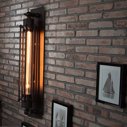 Industrial iron wall sconce with a vintage filament bulb mounted on a rustic brick wall next to framed nautical artwork in a loft-style interior.