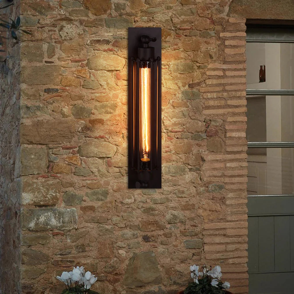 Black industrial iron wall sconce with a long vintage filament bulb mounted on a rustic stone wall, providing warm ambient lighting for a loft style.
