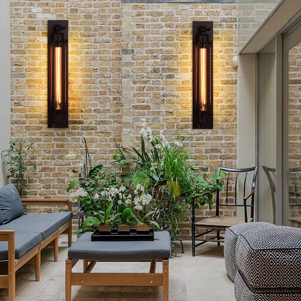Two black industrial iron wall sconces with vintage filament bulbs mounted on a rustic brick wall in a stylish loft-style indoor living space.