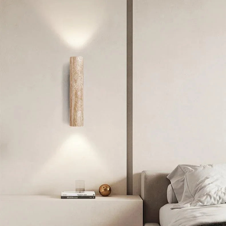 Travertine wall light casting warm light beside a bed
