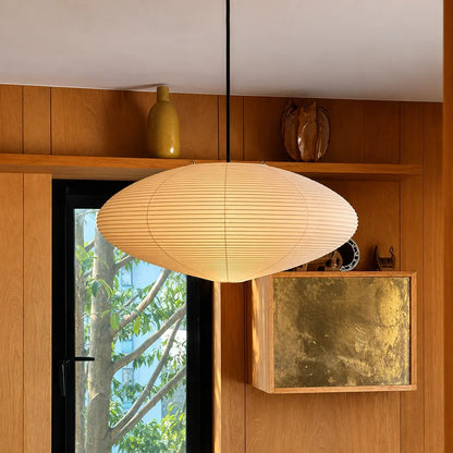Japanese oval rice paper pendant light suspended in a minimalist interior with wood-panelled walls, a window view and decorative shelf ornaments.