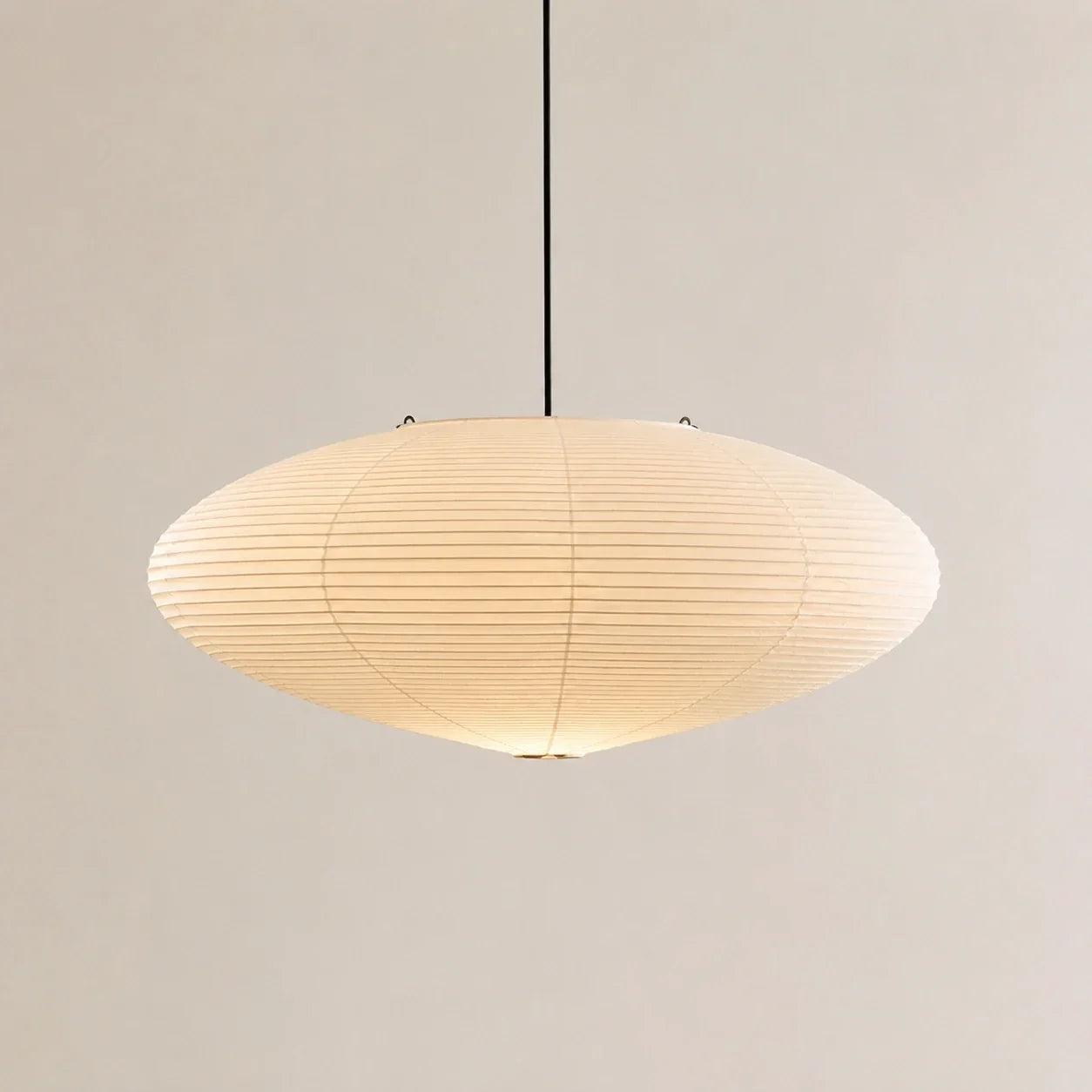 Minimalist Japanese oval pendant light featuring a textured white rice paper shade suspended by a thin black cord against a neutral background.