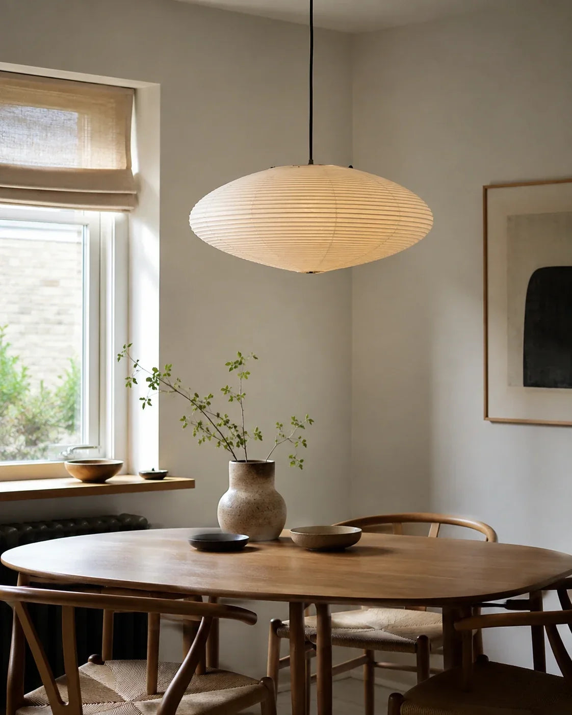 Japanese oval rice paper pendant light hanging above a minimalist wooden dining table in a bright, Japandi-style room with natural decor elements.