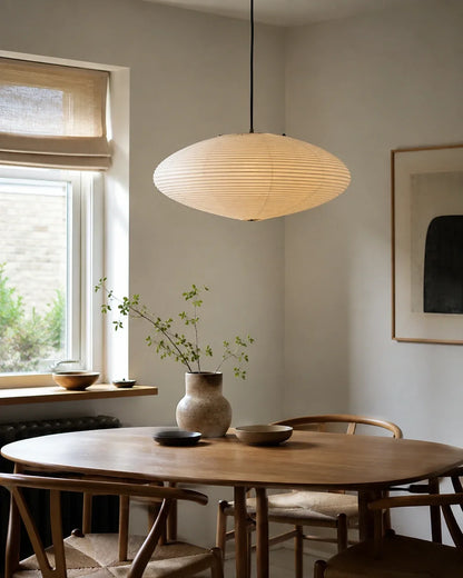Japanese oval rice paper pendant light hanging above a minimalist wooden dining table in a bright, Japandi-style room with natural decor elements.