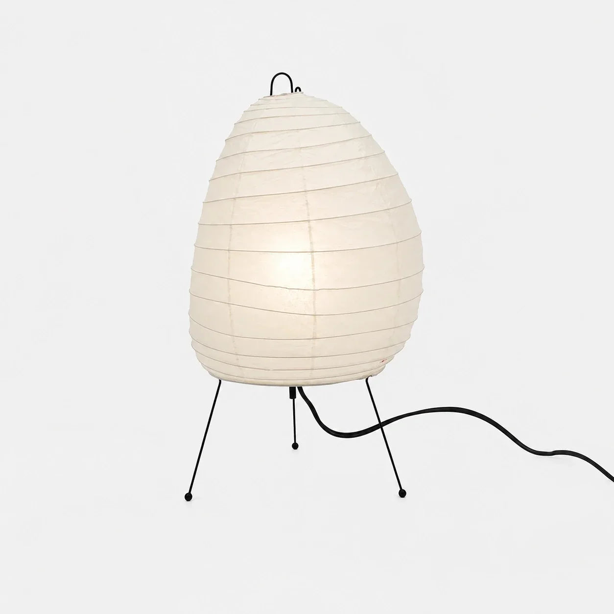Japanese-style rice paper table lamp with an organic, egg-shaped shade supported by a slim black tripod stand, providing soft ambient bedroom lighting.