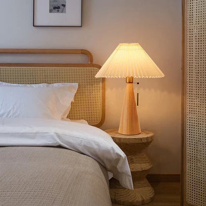 Wooden pleated table lamp beside a bed