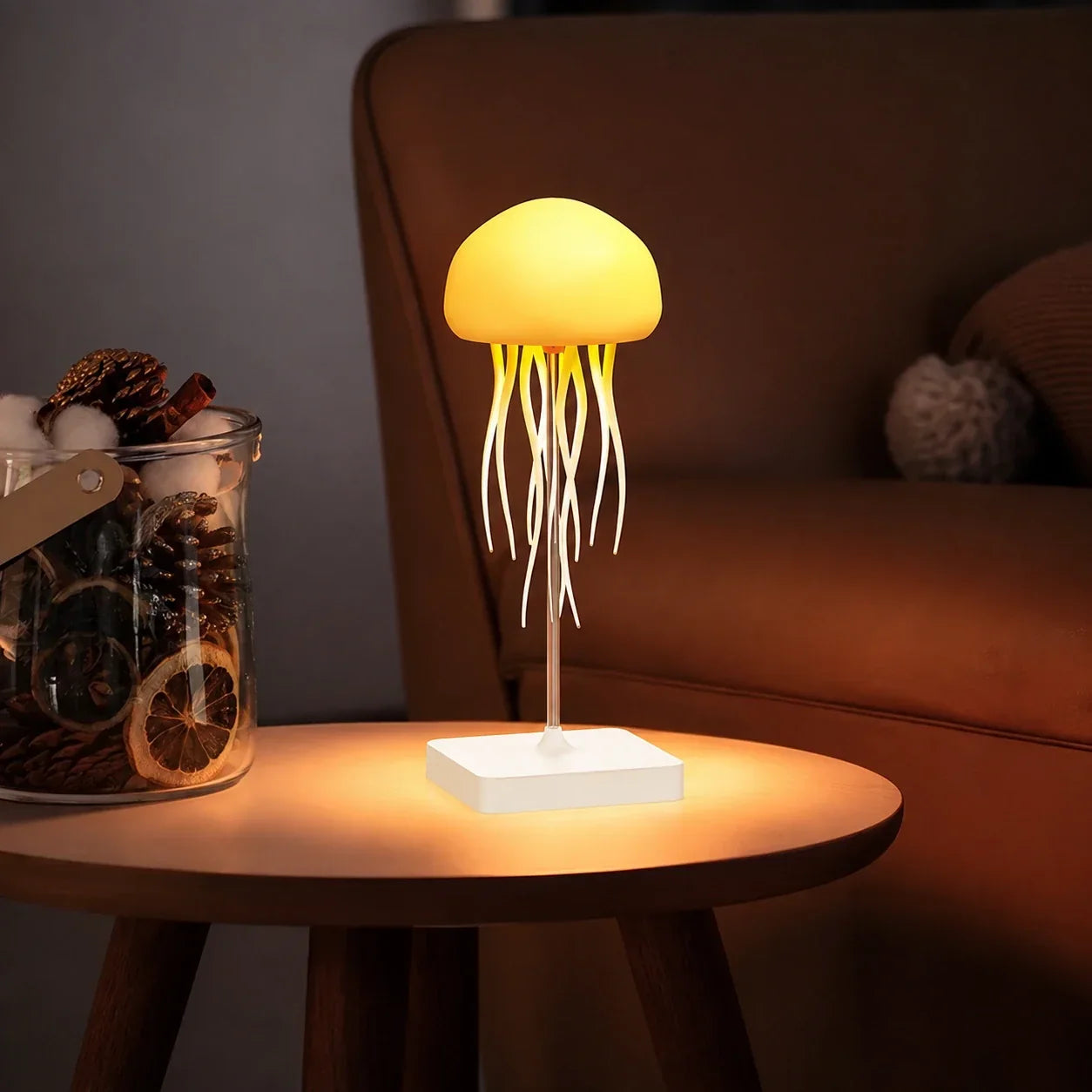 A jellyfish-shaped LED table lamp emitting a warm yellow glow on a wooden side table next to a decorative jar, creating a cosy ambient light.
