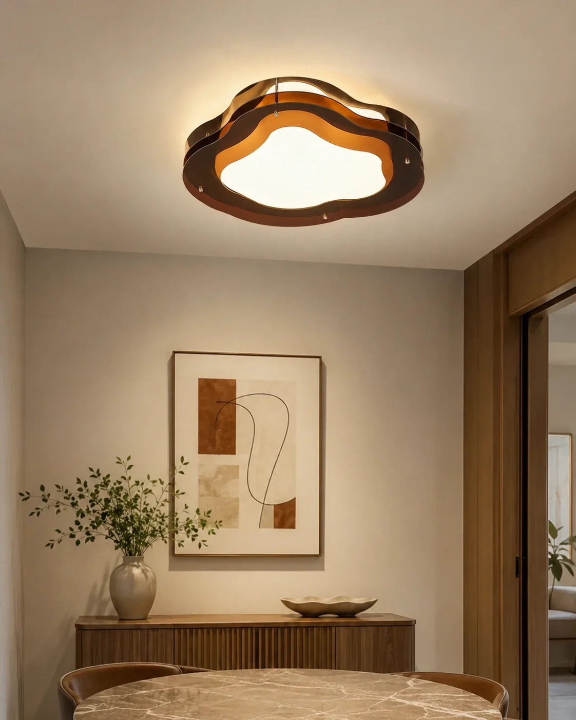 A modern cloud-shaped flush mount LED ceiling light with a layered design, casting a warm glow over a stylishly decorated dining area.