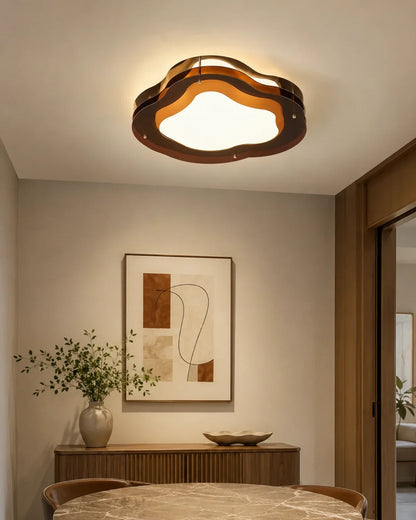 A modern cloud-shaped flush mount LED ceiling light with a layered design, casting a warm glow over a stylishly decorated dining area.