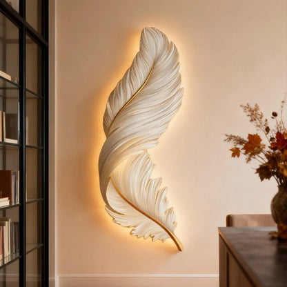 A modern white feather wall lamp with a gold spine, emitting a warm LED backlight onto a neutral wall to create cosy ambient lighting.