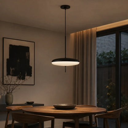 A modern black LED flying saucer pendant light hanging above a round wooden dining table in a warm, contemporary dining room setting.