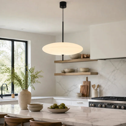 Modern white flying saucer LED pendant light suspended over a marble kitchen island in a bright, Nordic-style kitchen with wooden shelving.