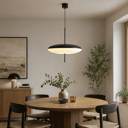 Modern black flying saucer LED pendant light suspended over a round wooden dining table in a minimalist Nordic style living space.