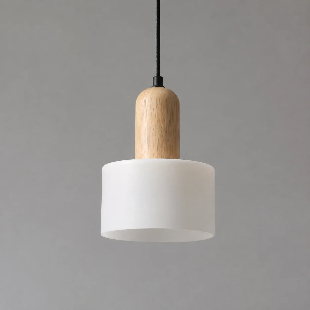 Minimalist pendant light featuring a cylindrical white marble shade with a natural wood top detail, suspended by a slim black cable against a grey backgrou