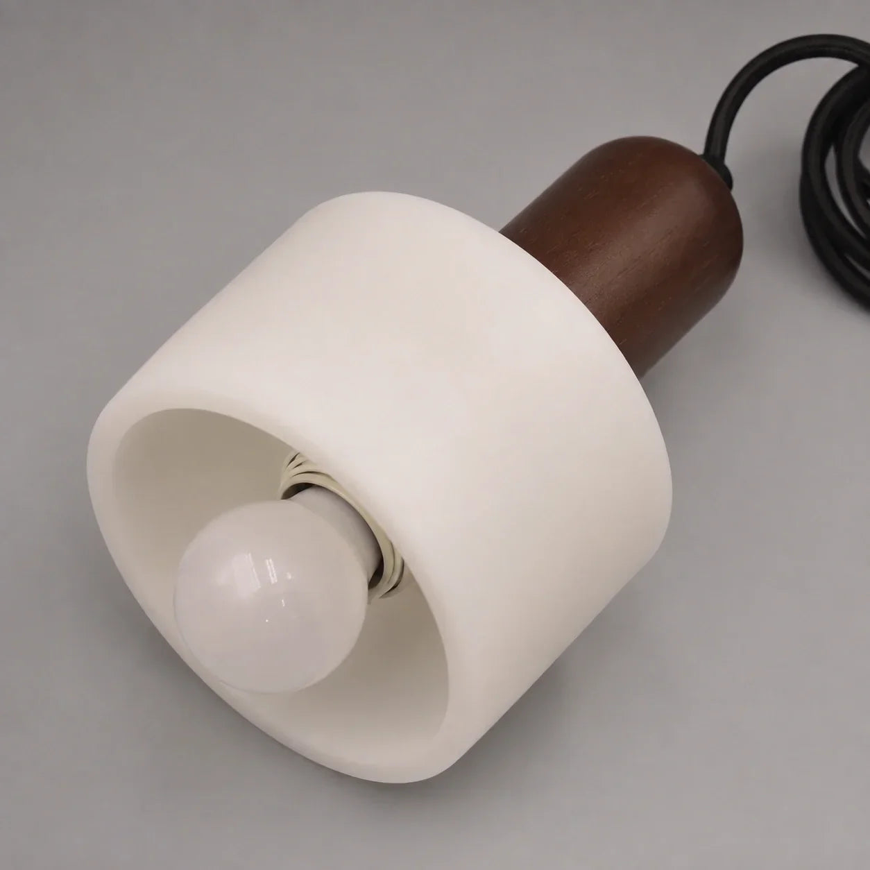 Minimalist pendant light featuring a cylindrical white marble shade paired with a dark wood top detail and a black cable against a neutral background.