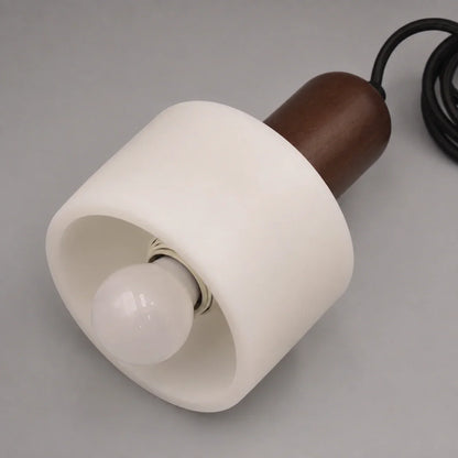 Minimalist pendant light featuring a cylindrical white marble shade paired with a dark wood top detail and a black cable against a neutral background.