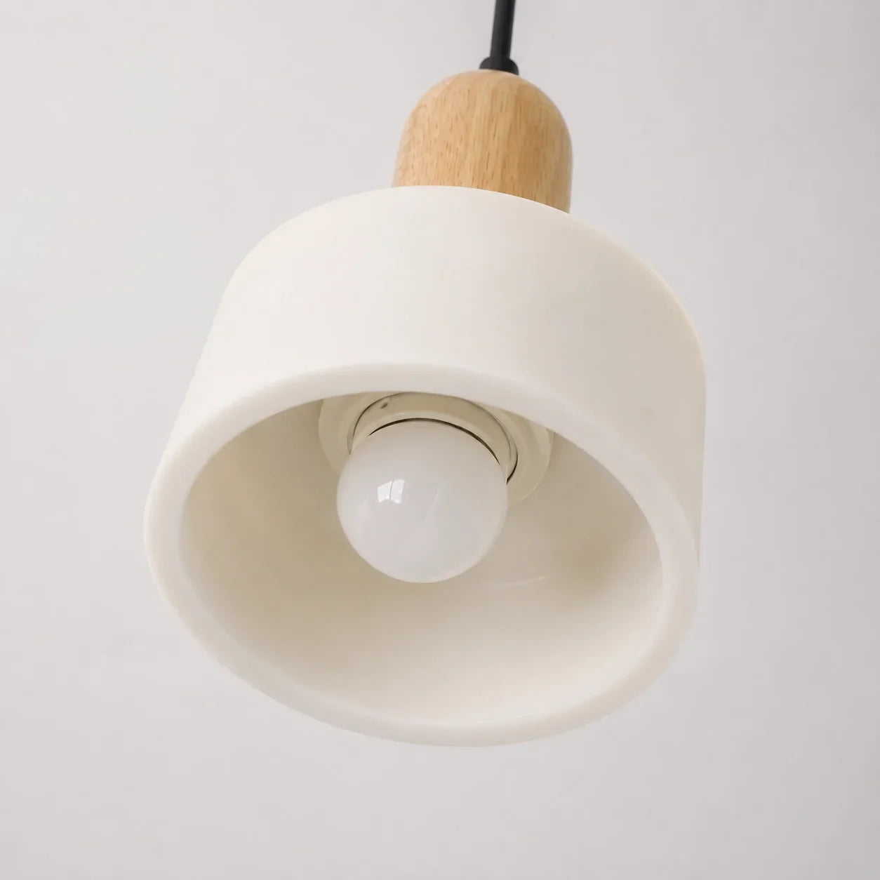 Minimalist pendant light featuring a smooth white marble shade with a natural wood top detail and a single globe bulb, suspended by a black cable.