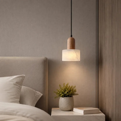 Minimalist pendant light featuring a cylindrical marble shade and wood detail, hanging above a bedside table in a contemporary bedroom interior.