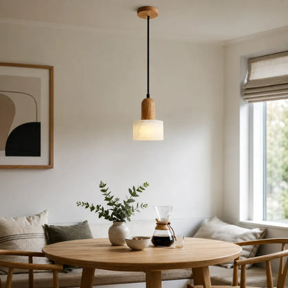 Minimalist marble pendant light with natural wood detailing hanging above a round wooden dining table in a bright, modern interior living space.