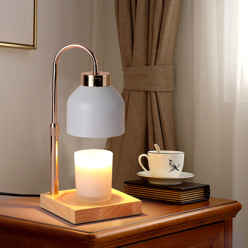 White matte candle warmer lamp with an adjustable brass-style arm beside books