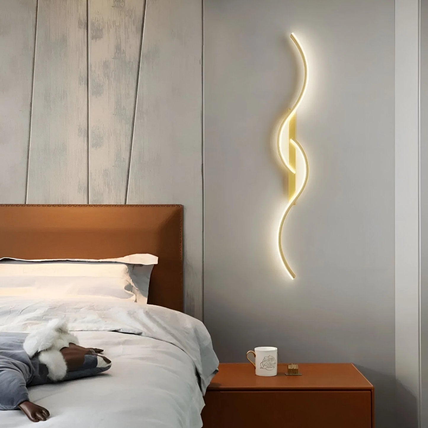 Minimalist curved LED wall light with a warm glow mounted on a grey bedroom wall above a bedside table, creating a modern and elegant atmosphere.