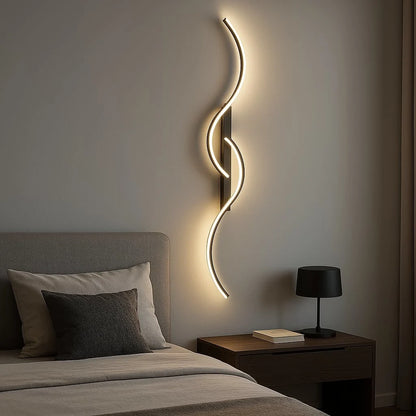 A minimalist curved LED wall light with a sleek, wave-like design mounted above a bedside table in a modern bedroom, casting a warm, ambient glow.