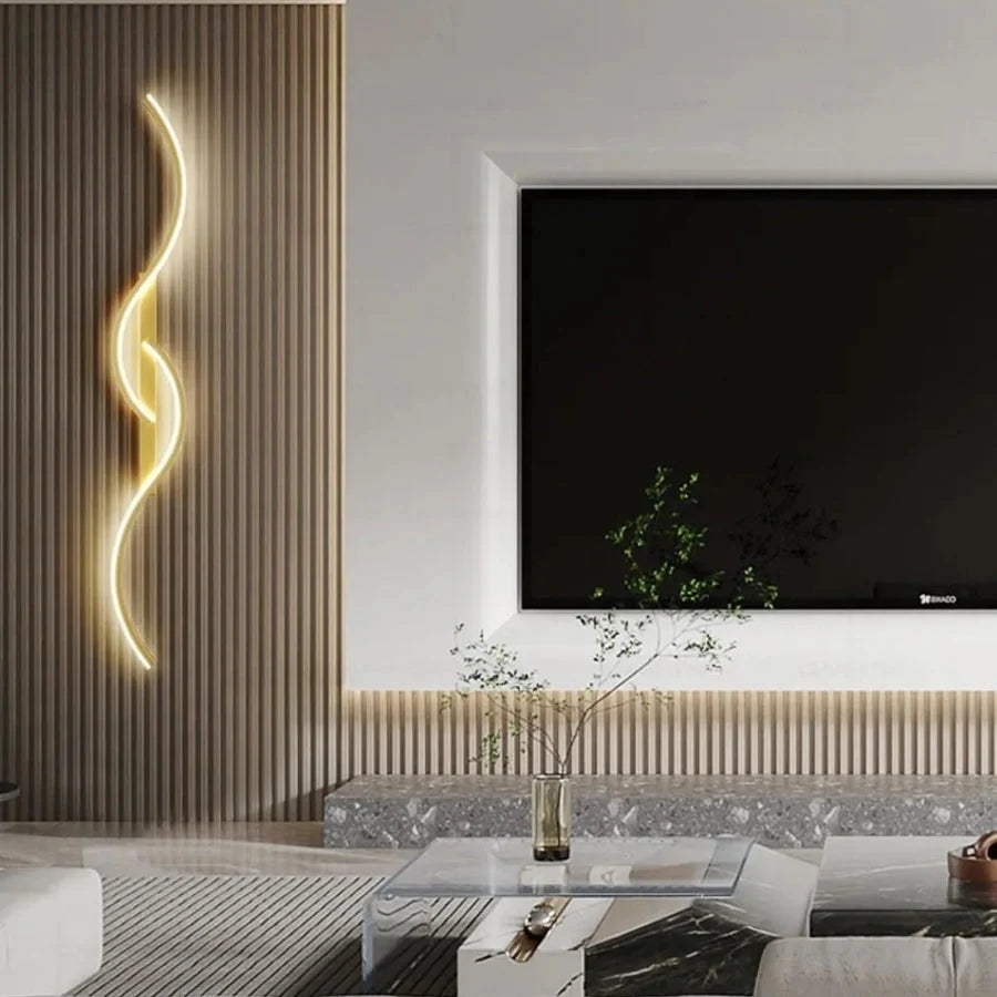 Minimalist curved LED wall light with a sleek gold finish mounted on a textured wooden slat wall in a modern living room next to a television screen.