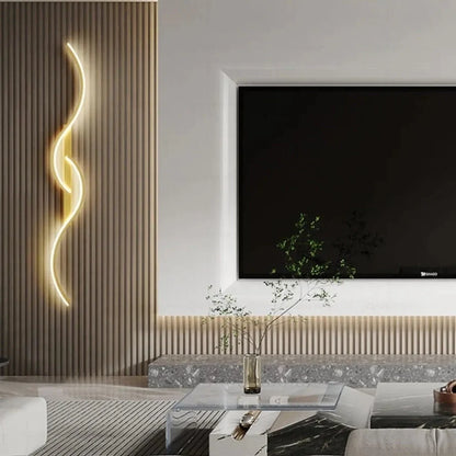 Minimalist curved LED wall light with a sleek gold finish mounted on a textured wooden slat wall in a modern living room next to a television screen.