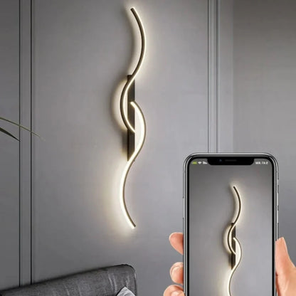 A minimalist curved LED wall light mounted on a grey wall, being captured on a smartphone screen held in a hand to demonstrate modern indoor lighting.