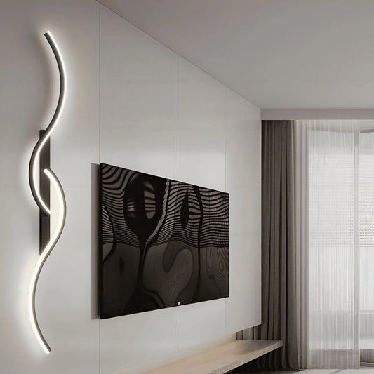 A minimalist curved LED wall light with a sleek, serpentine design mounted on a white wall next to a television in a modern living room interior.