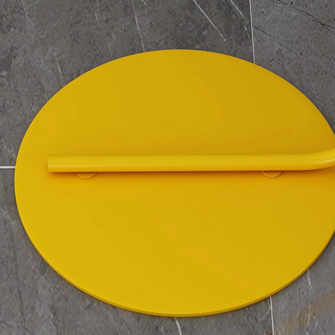 Close-up of the circular yellow metal base and lower stem of the minimalist LED arc floor lamp, resting on a grey tiled floor.